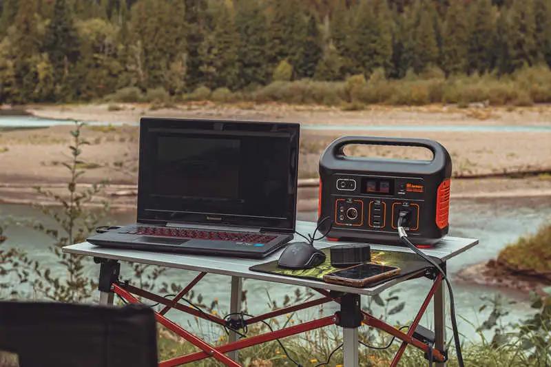 laptop and power bank on table next to a stream outside