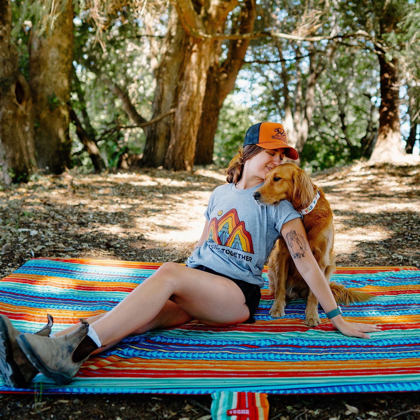Woman sitting on a colorful blanket with a dog in a forest setting