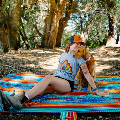Woman sitting on a colorful blanket with a dog in a forest setting