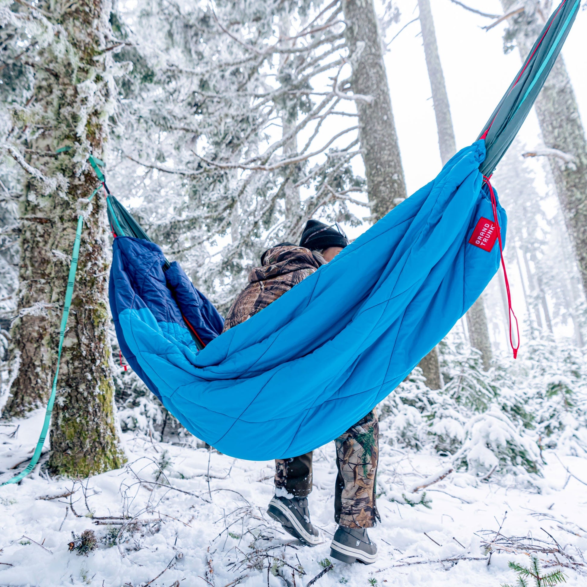 Person in a blue hammock in a snowy forest