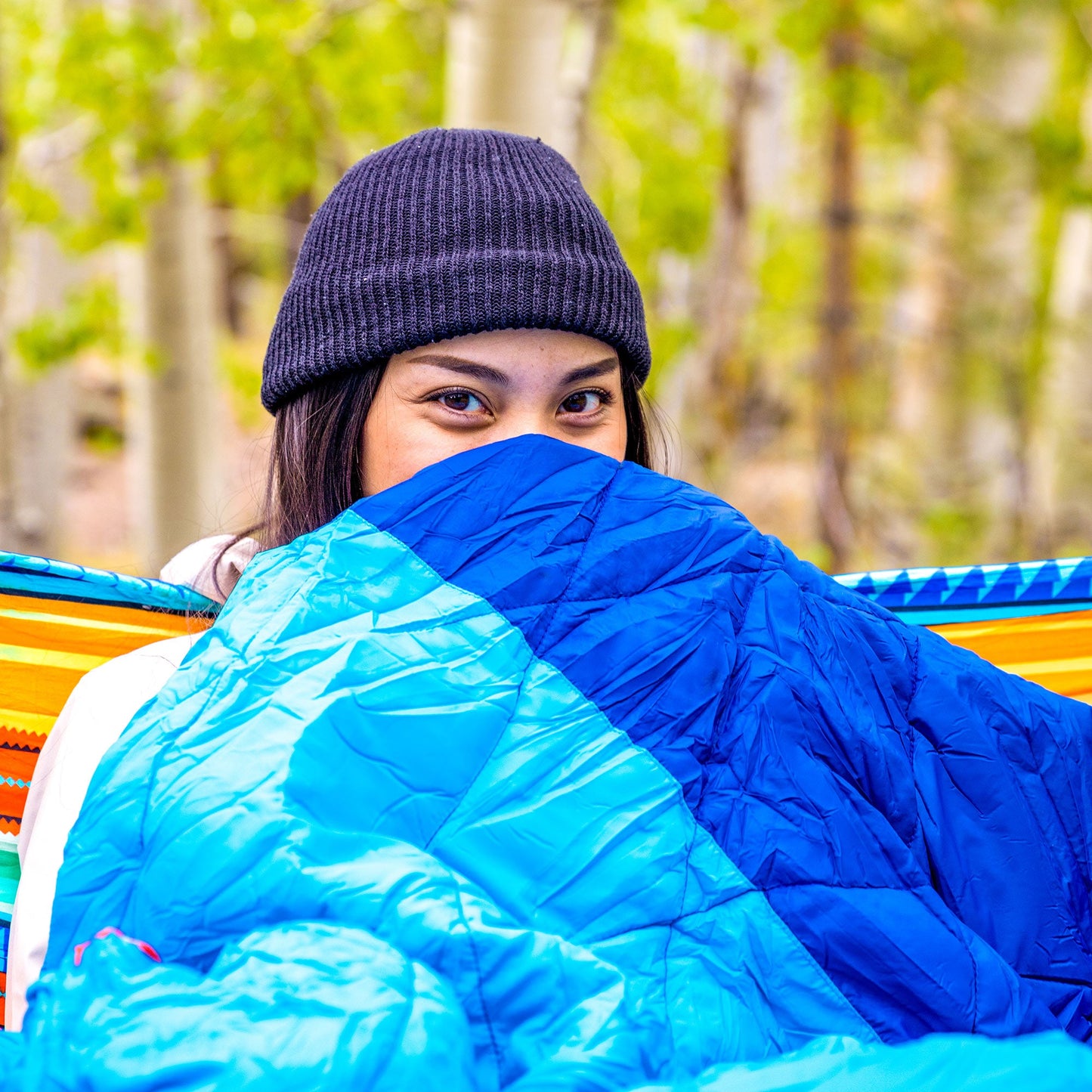 Person wrapped in a blue sleeping bag with a forest background