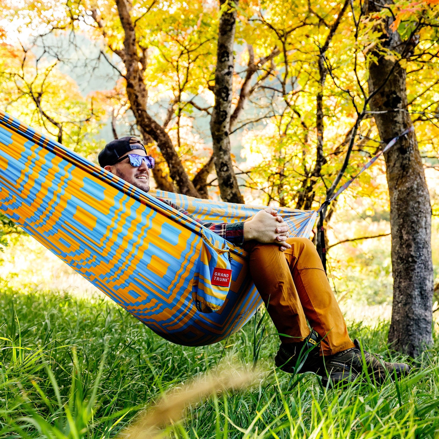Person relaxing in a colorful hammock surrounded by trees with autumn foliage.