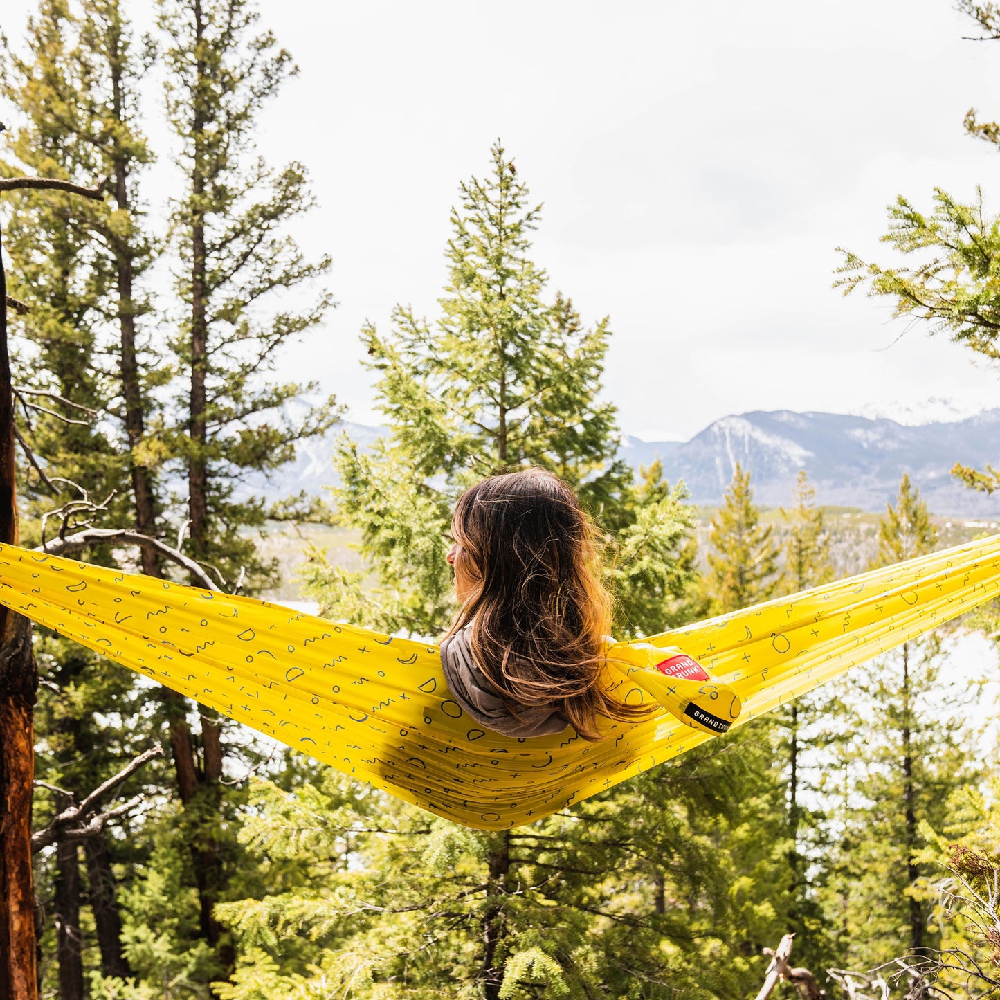 Person relaxing in a yellow hammock surrounded by trees and mountains