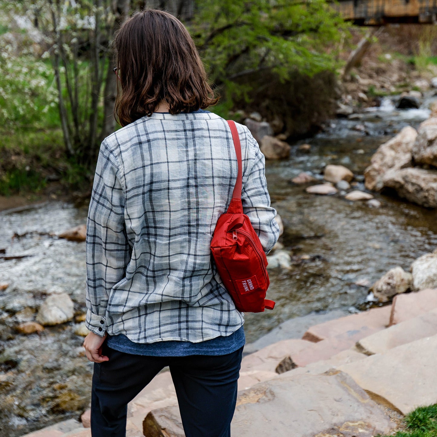 Person with a red bag standing by a stream in a natural setting