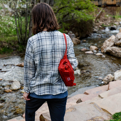 Person with a red bag standing by a stream in a natural setting